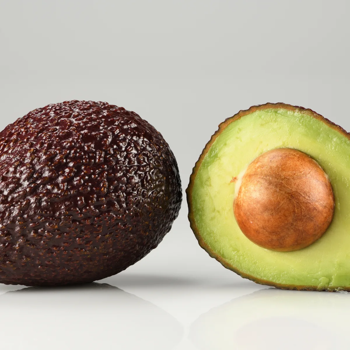 Whole and halved ripe Hass avocados showing dark pebbled skin